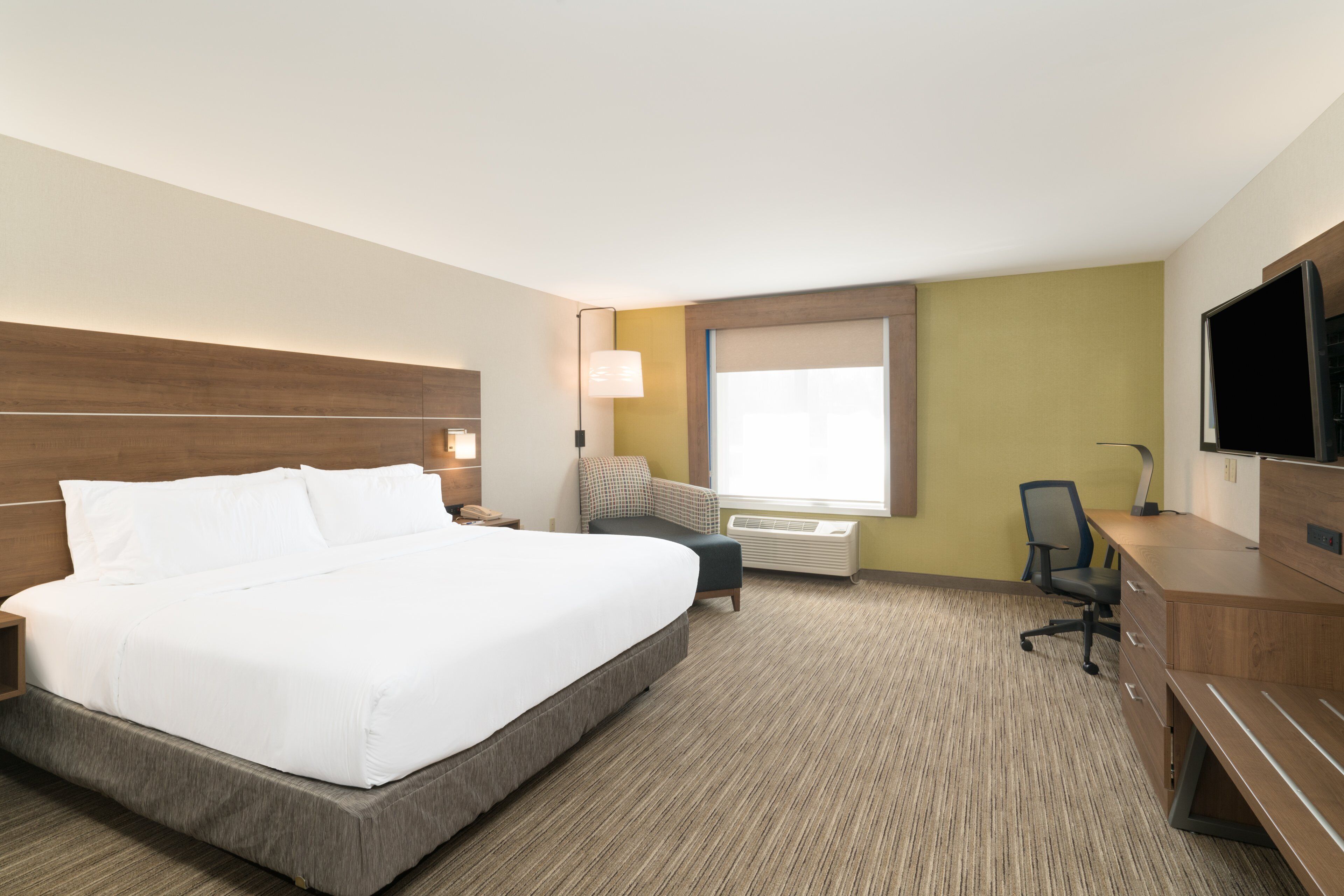 Ein Hotelzimmer mit einem großen Bett, einem Schreibtisch, einem Sessel, einem Fernseher und einem Fenster mit Jalousien.