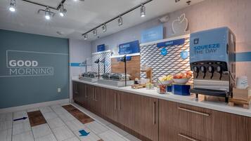 A modern breakfast area with a counter, coffee machine, and fruit display.