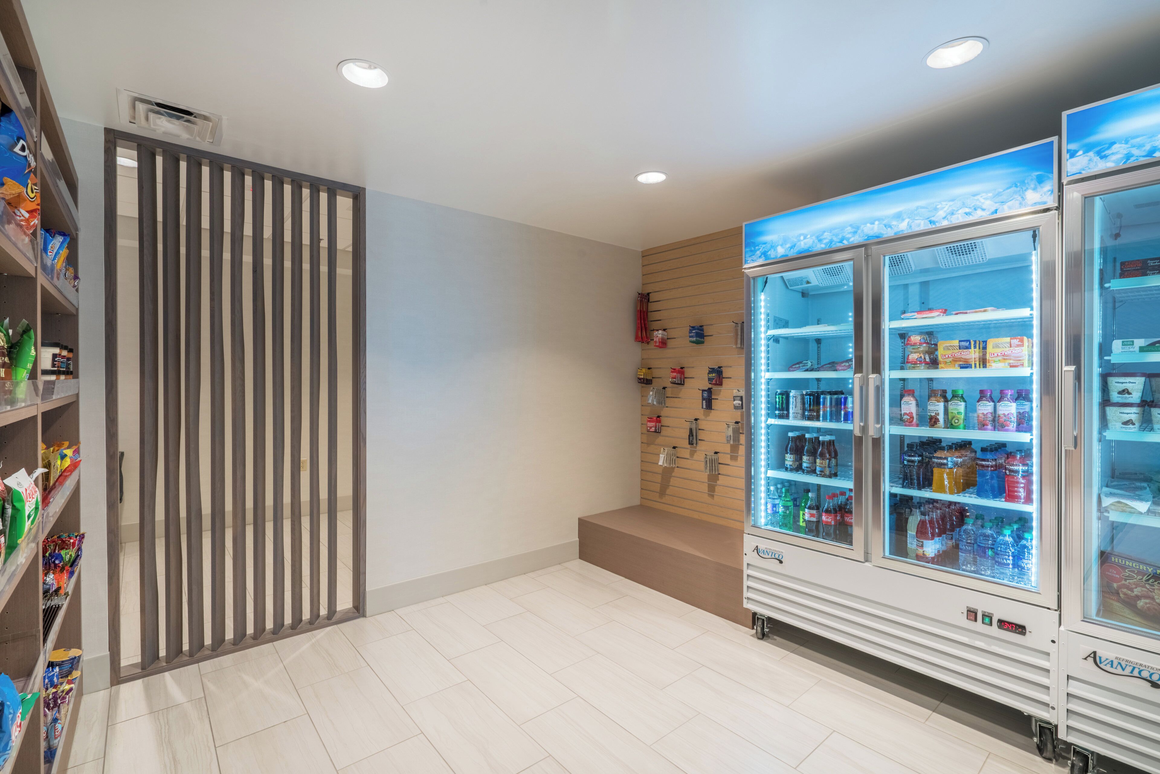 A clean, modern room with a vending machine stocked with snacks and drinks, a wooden panel wall, and a tiled floor.