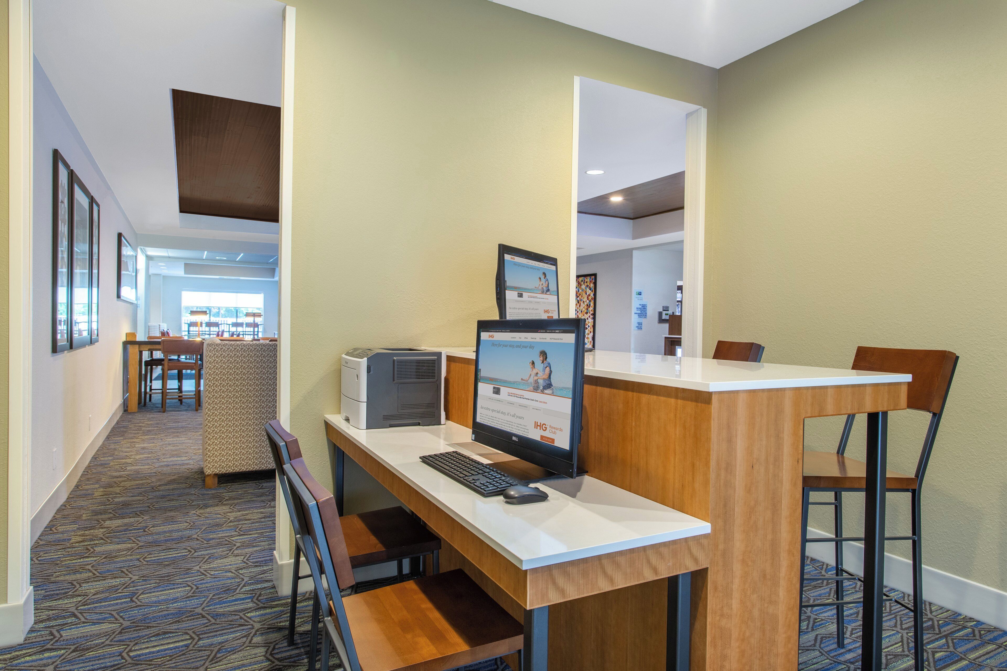 A hotel reception desk with a computer, a printer, and a seating area with chairs and a small table.