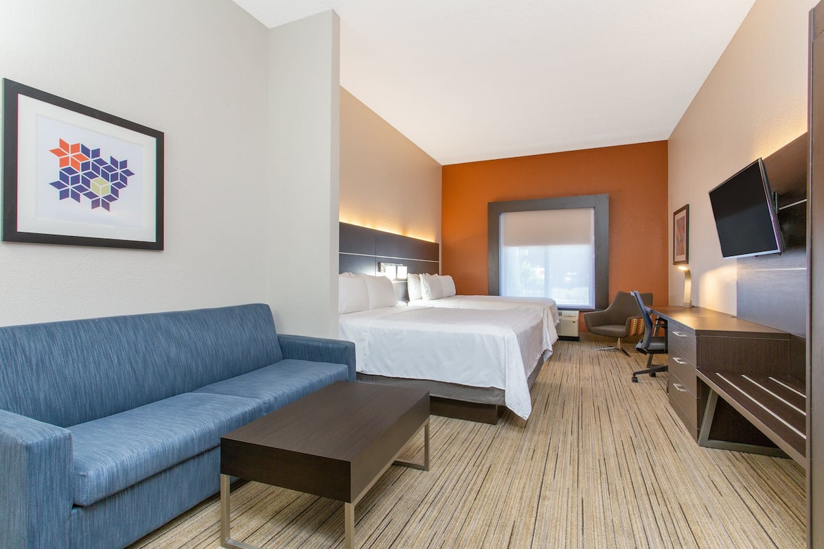 A hotel room with a bed, a blue sofa, a desk, and a television.