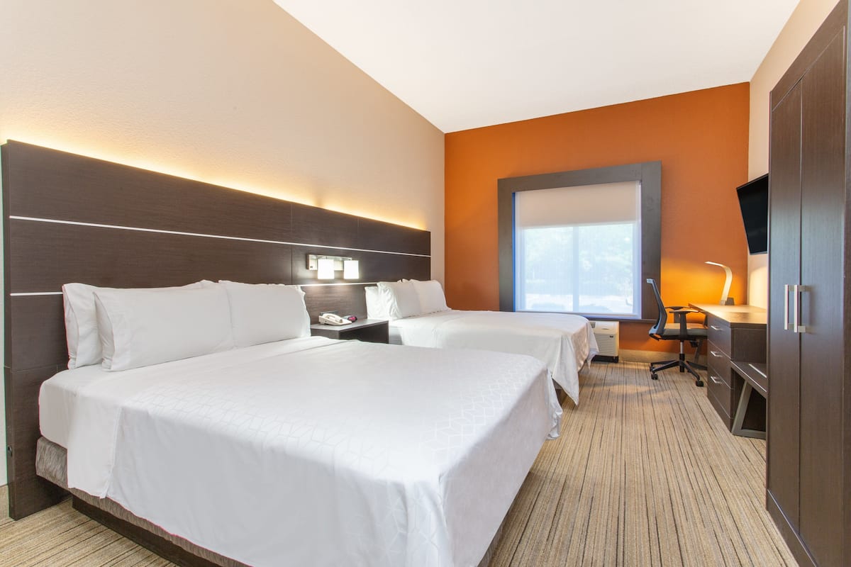 A hotel room with two beds, a desk, a chair, a TV, and a window.