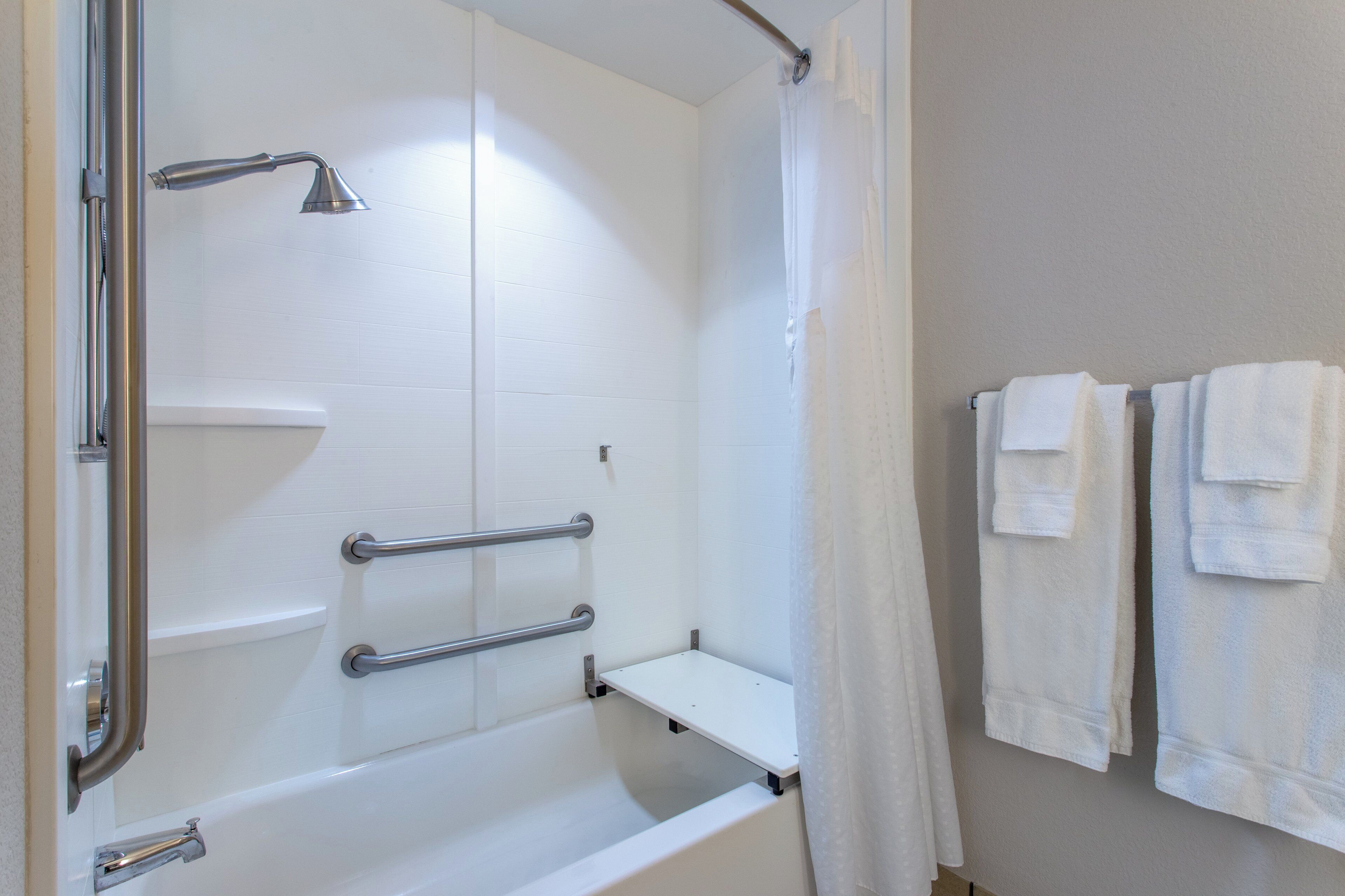 A shower with a handheld showerhead, grab bars, and a white bathtub.