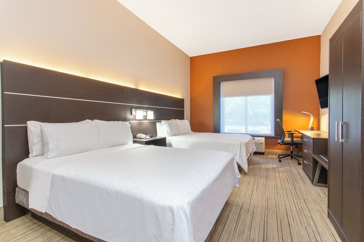 A hotel room with two beds, a desk, a chair, a television, and a large window.