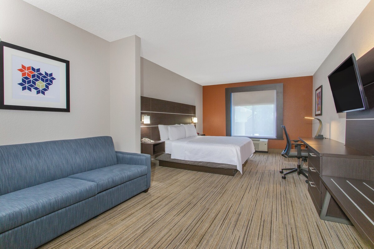A hotel room with a bed, a sofa, a desk, a TV, and a window.