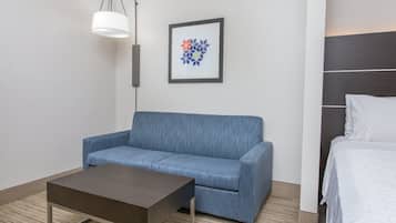 Een hotelkamer met een blauwe bank, een kleine tafel, een bed, een lijst met een foto aan de muur en een lamp.