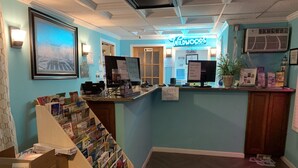 A reception area with a counter, a sign for Wildwoods by the Sea, a wall-mounted air conditioner, and a display of magazines. - Sandy Shores Resort Motel (North Wildwood)