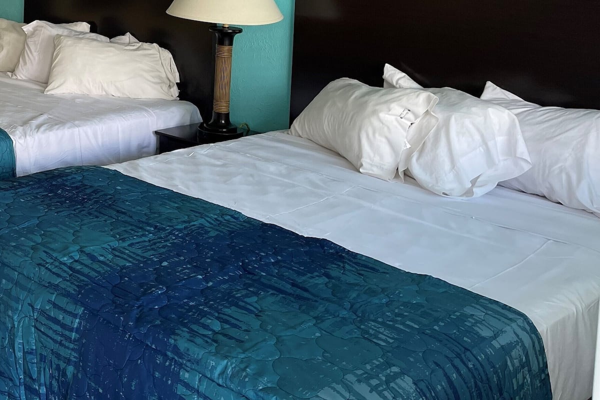 Ein Hotelzimmer mit zwei Betten, einem Nachttisch mit Lampe und Bildern von Strandmotiven.