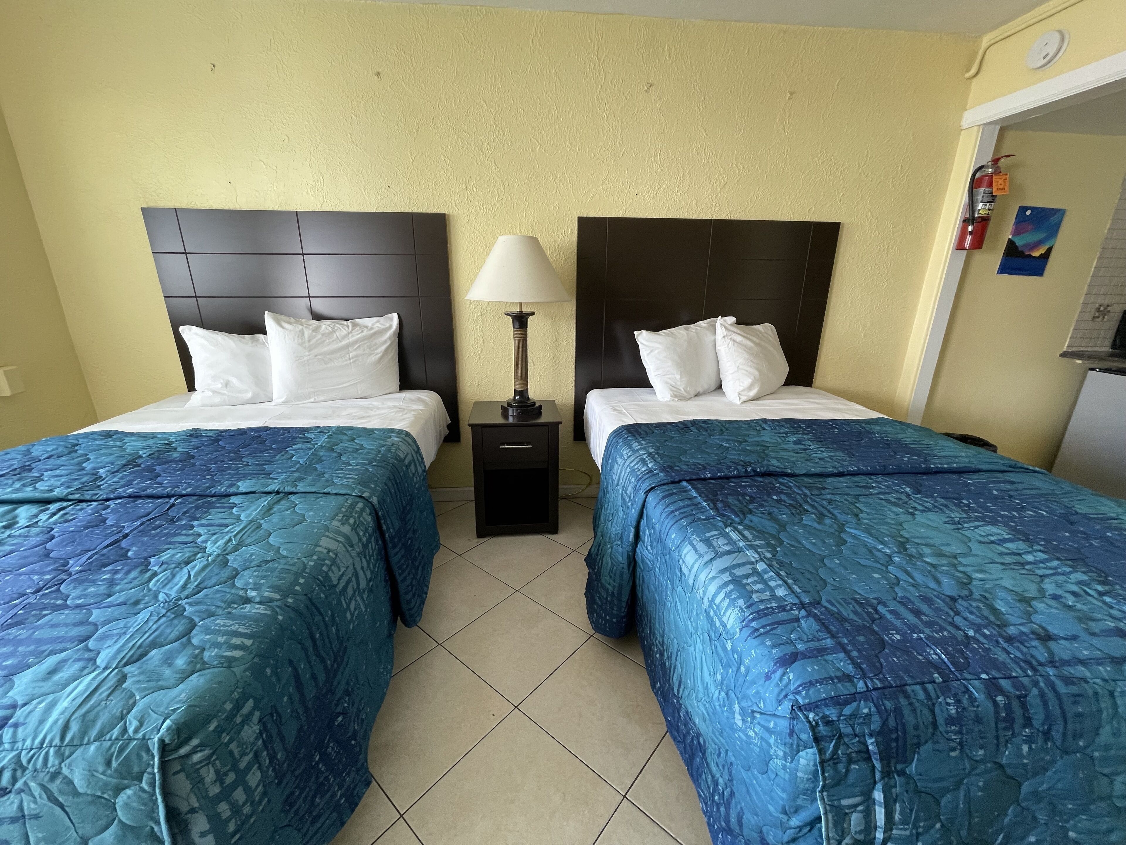 A hotel room with two beds, each with a headboard, a nightstand with a lamp, and a small table.