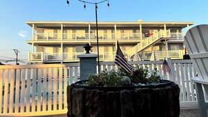 A multi-story hotel with balconies, a stone planter with plants, and string lights. - Sandy Shores Resort Motel (North Wildwood)