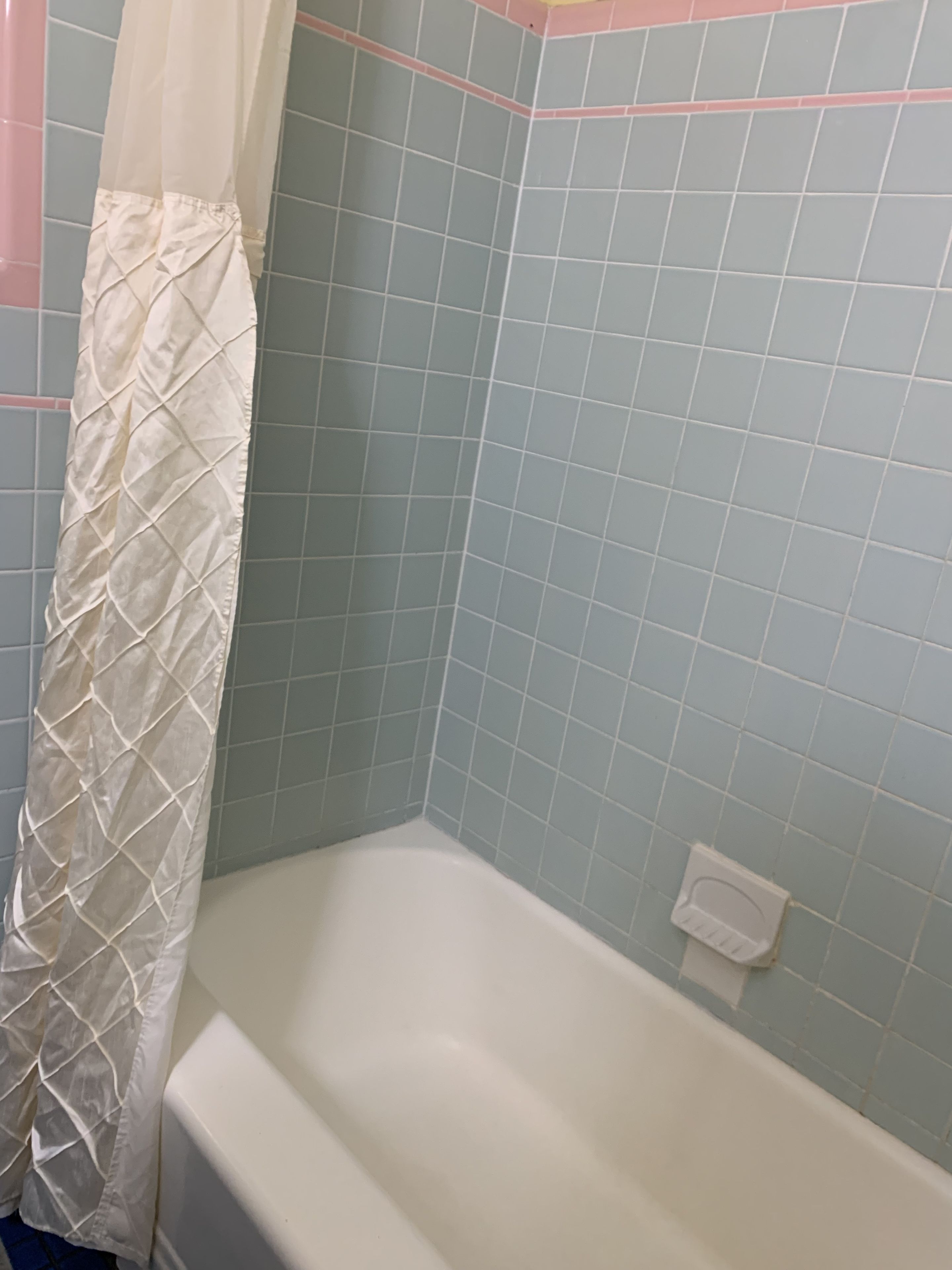 Ein Badezimmer mit einer weißen Badewanne, hellblauen Fliesenwänden und einem weißen Duschvorhang.