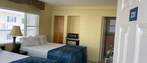 A hotel room with two beds, a desk with a lamp, a microwave, and a door marked with the number 231.