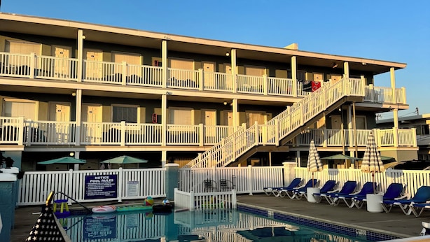 A multi-story hotel with a pool area, including lounge chairs and umbrellas. - Sandy Shores Resort Motel (North Wildwood)