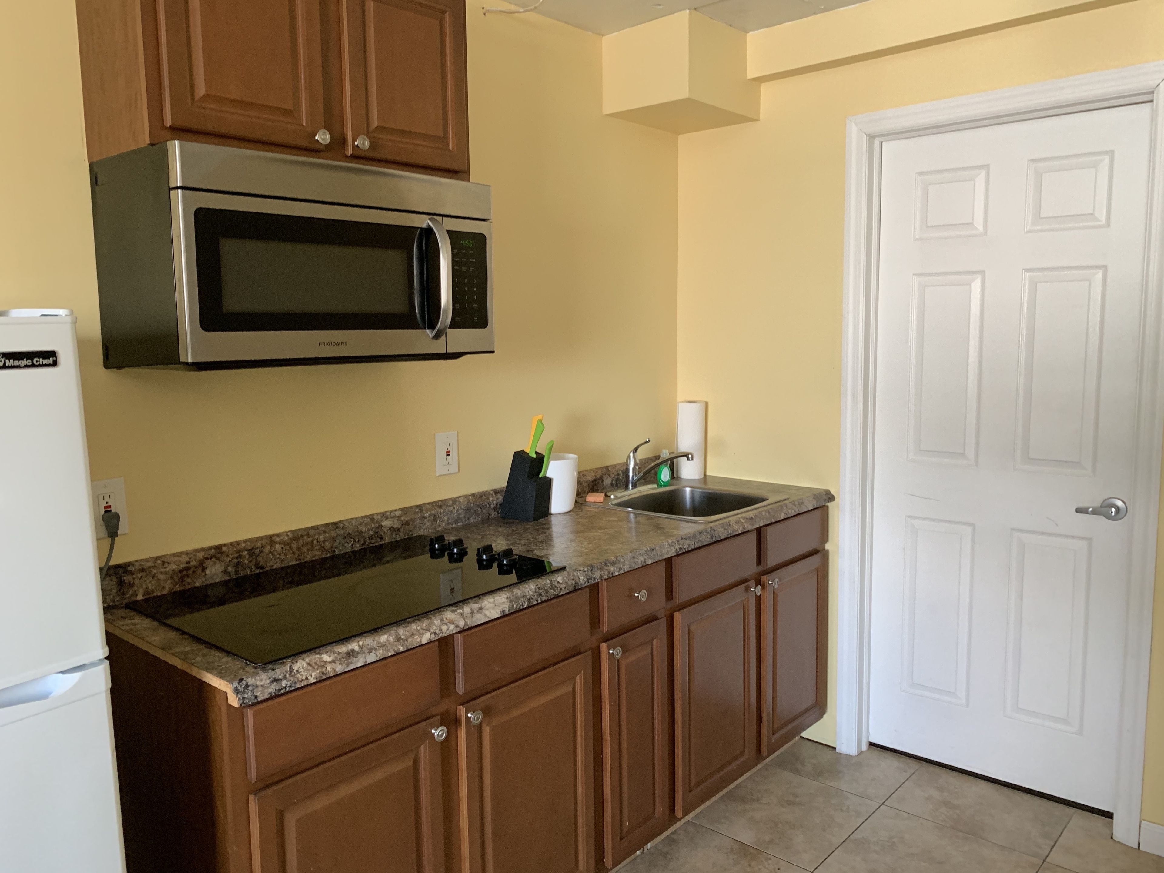 A kitchen with a stainless steel microwave, granite countertop, wooden cabinets, a sink, and a white door.