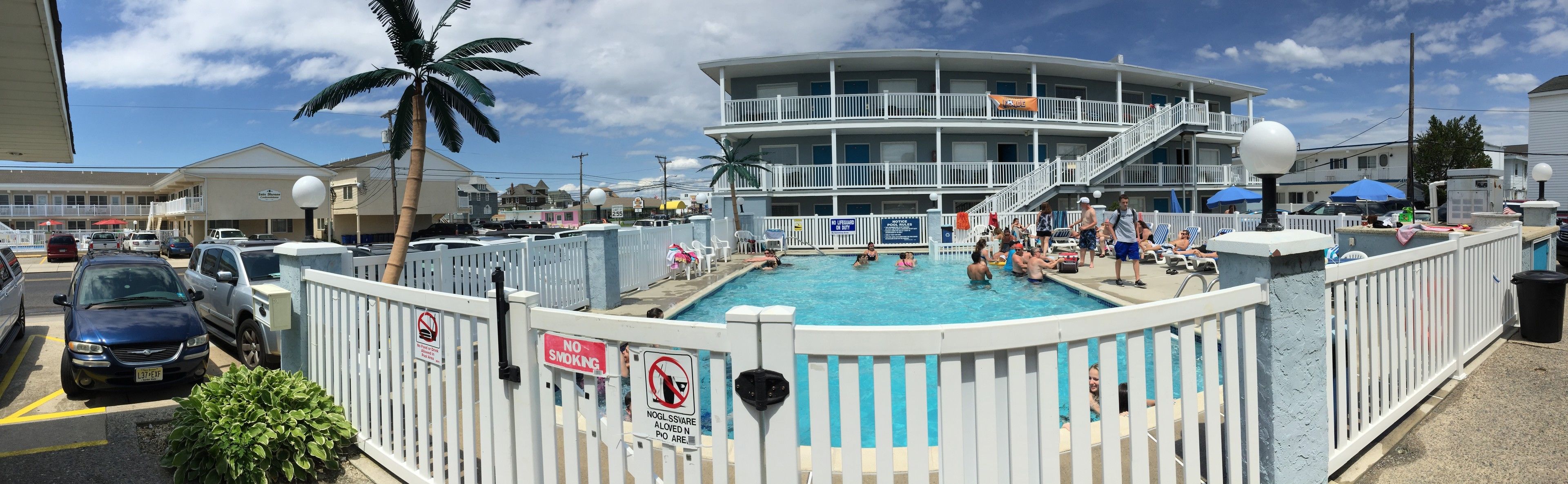 A pool area with a white fence, a no smoking sign, and a no lifeguard on duty sign.