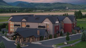 A multi-story building with a prominent "Residence Inn by Marriott" sign, featuring a parking lot and a view of surrounding green hills. - Residence Inn by Marriott Bozeman (Bozeman)