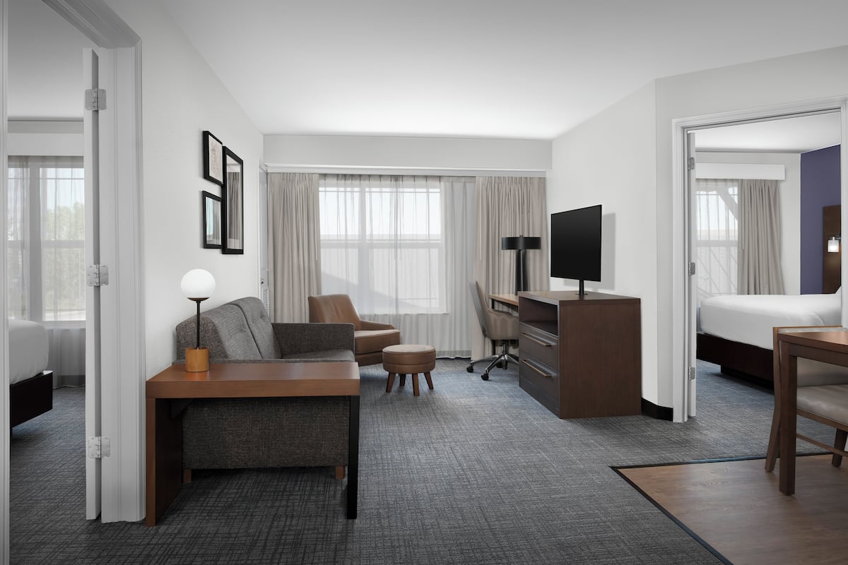 A hotel room with a bed, a desk, a chair, a sofa, and a TV.