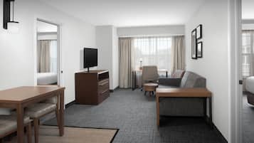 A hotel room with a wooden desk, a sofa, a TV, and a window with curtains.