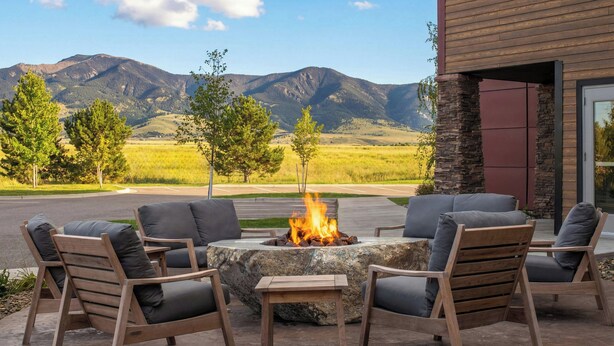 An outdoor seating area with a fire pit, surrounded by stone walls and wooden furniture, overlooking a mountainous landscape. - Residence Inn by Marriott Bozeman (Bozeman)