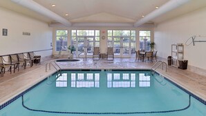 An indoor swimming pool with clear blue water, surrounded by lounge chairs and tables, large windows, and a tiled floor. - Residence Inn by Marriott Bozeman (Bozeman)