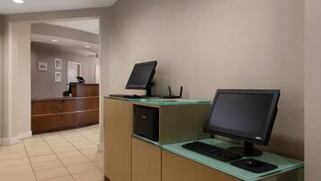 A reception desk with two computer monitors, a keyboard, and a mouse. There is a reception area with a counter and a door in the background.