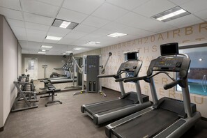 Ett gym med löpband, styrketräningsmaskiner och en vägg täckt med speglar.