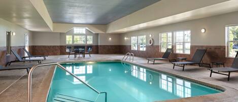 An indoor swimming pool with a tiled floor, a pool ladder, and lounge chairs around the pool.