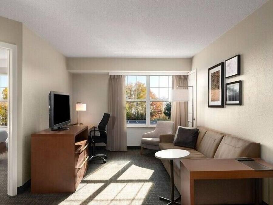 A hotel room with a bed, desk, chair, sofa, TV, and large windows.