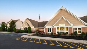 A hotel with a prominent American flag, a parking lot with marked spaces, and a well-maintained exterior with brick and siding. - Residence Inn by Marriott Mt. Laurel at Bishop's Gate (Mount Laurel)