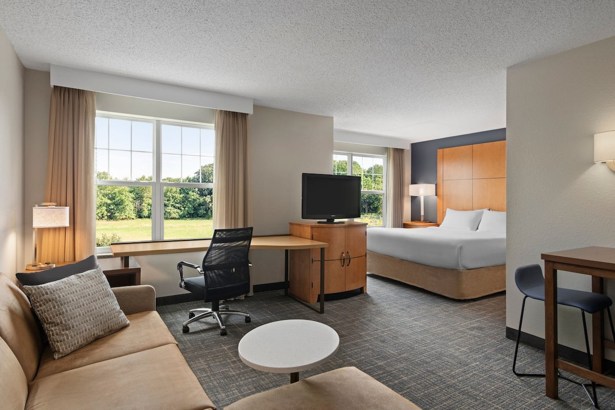 A hotel room with a bed, a desk with a TV, a chair, a sofa, and a small table.