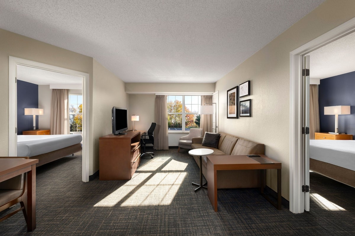 A hotel room with a bed, desk, chair, sofa, and TV.
