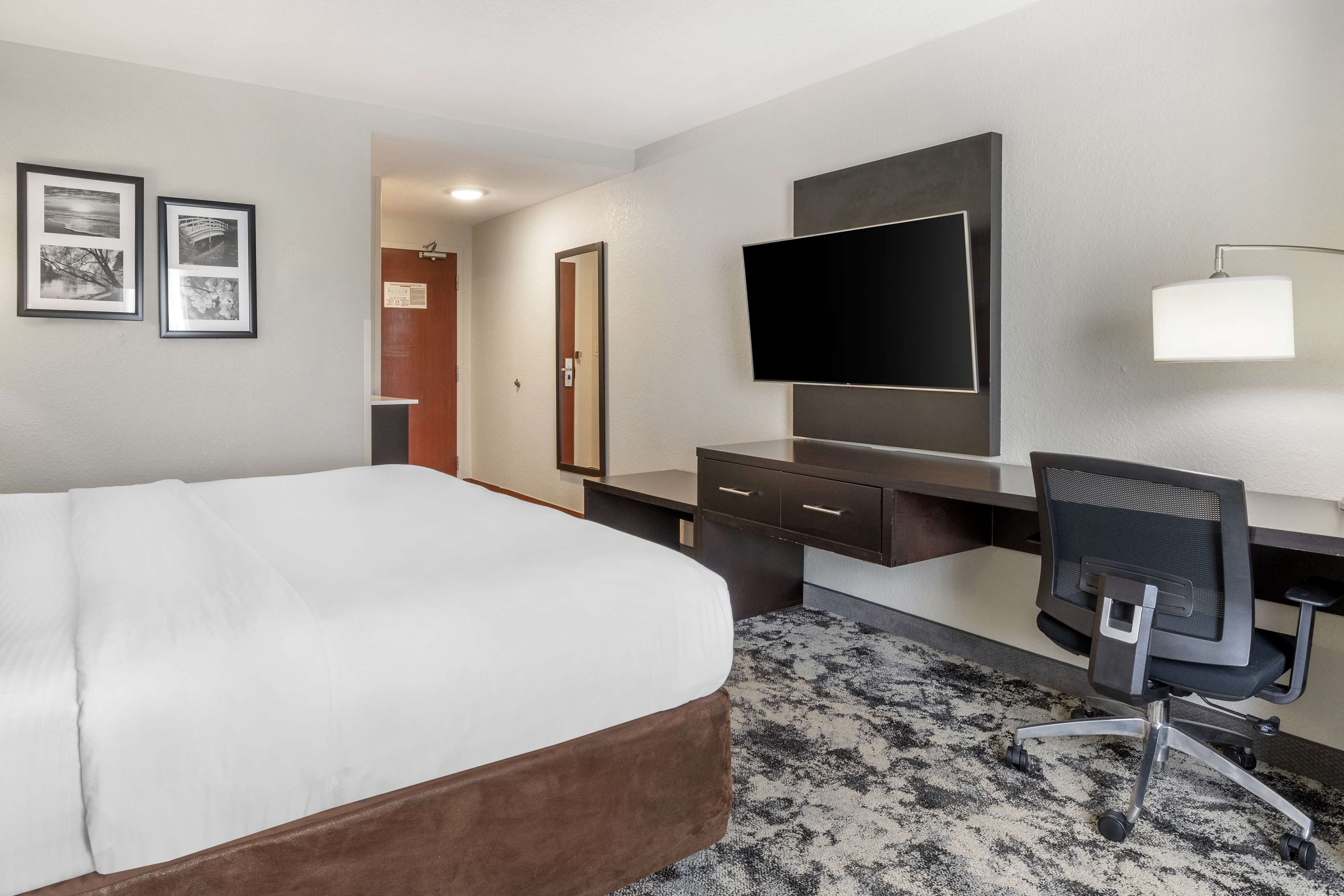 A hotel room with a bed, a desk with a computer, a TV, and framed pictures on the wall.