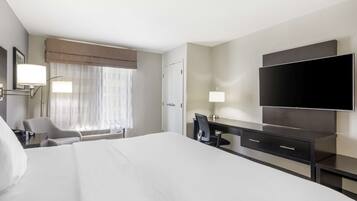 Habitación de hotel con una cama grande, un escritorio con silla, un televisor de pantalla plana montado en la pared y una ventana con cortinas traslúcidas.
