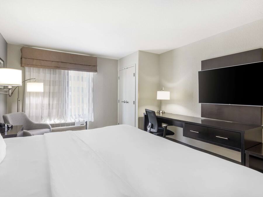 Habitación de hotel con una cama grande, un escritorio con silla, un televisor de pantalla plana montado en la pared y una ventana con cortinas traslúcidas.