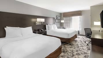 A hotel room with two beds, a desk, a chair, and a large window with curtains.