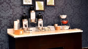 Ein Hotel-Rezeptionsbereich mit dunkel gemustertem Wandpapier, einer weißen Rezeption mit verschiedenen Annehmlichkeiten und gerahmten botanischen Drucken an der Wand.