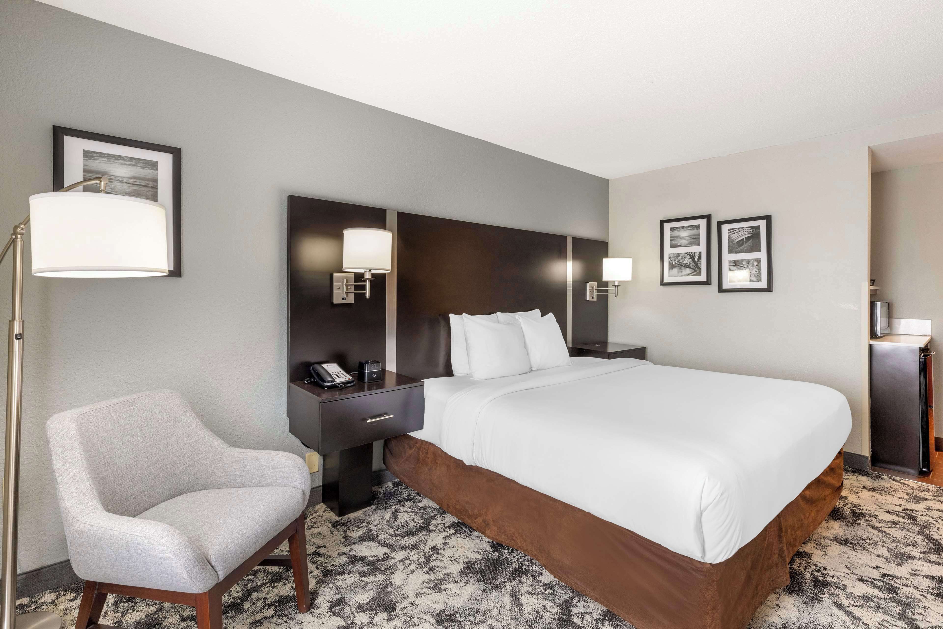 Een hotelkamer met een groot bed, een stoel, een bureau met telefoon, en wandlampen.