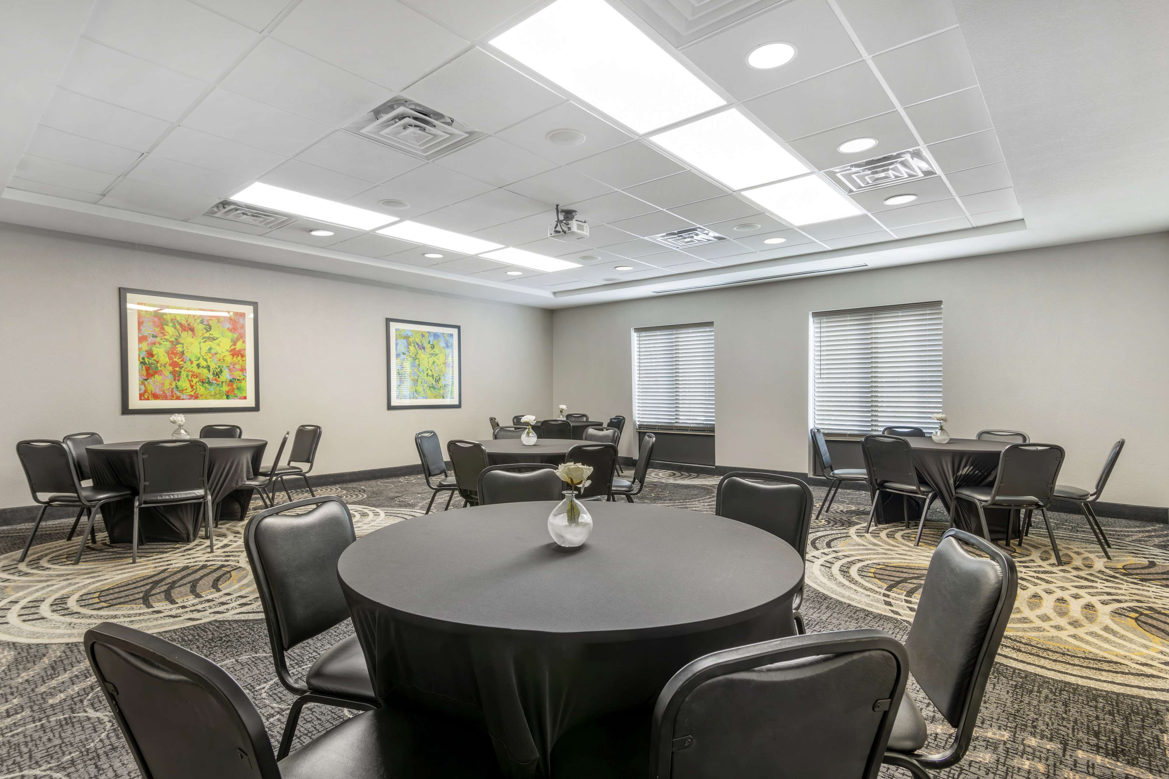 A conference room with round tables, black chairs, and a carpeted floor.