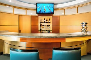 Zona de bar con televisor sobre la barra, estante con botellas y dos taburetes azules.