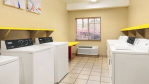 A laundry room with four white washers and dryers, a yellow table, and two abstract paintings on the wall. - Candlewood Suites Augusta by IHG (Augusta)
