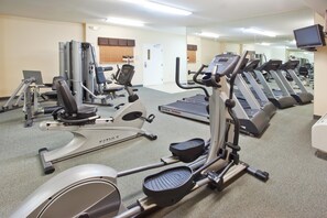 A gym with various exercise machines, a mirrored wall, and a door in the background. - Candlewood Suites Augusta by IHG (Augusta)
