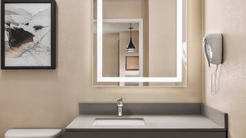 A bathroom with a white toilet, a gray sink, a framed abstract painting, a mirror, and a telephone.