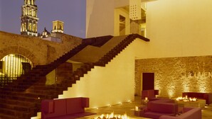 A modern lounge area with a stone wall, a fire pit, and a staircase leading to an upper level. - La Purificadora, Puebla, a Member of Design Hotels (Puebla)