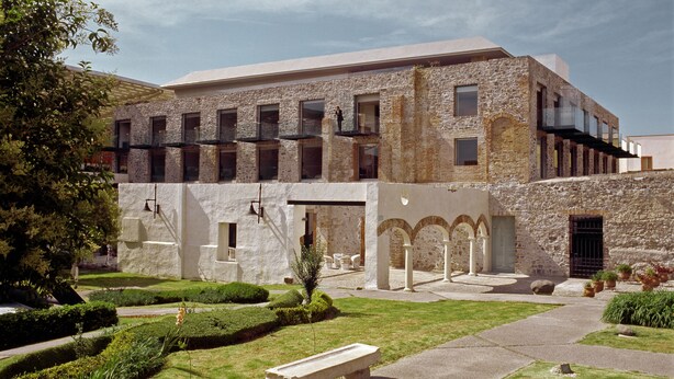 A building with a stone facade, multiple windows, and a courtyard with a bench and greenery. - La Purificadora, Puebla, a Member of Design Hotels (Puebla)