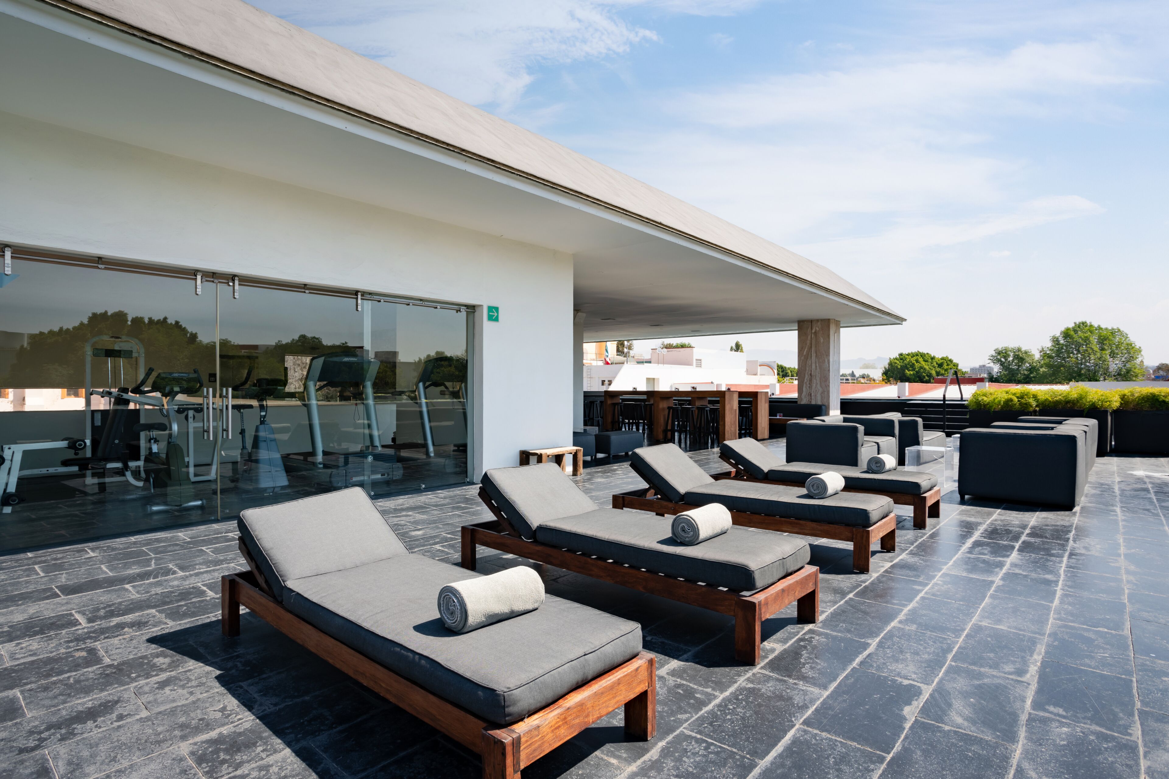 A rooftop lounge area with sun loungers, a glass door entrance, and a view of the surrounding buildings.