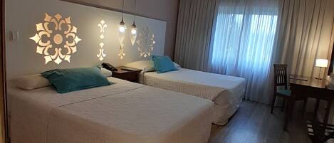 Habitación de hotel con dos camas, un ventilador de techo, una mesa de comedor con sillas y lámparas de pared decorativas.