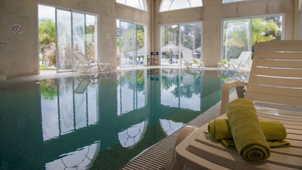 Une piscine intérieure avec des parois en verre transparent, des chaises longues et une serviette posée sur l’une d’elles.