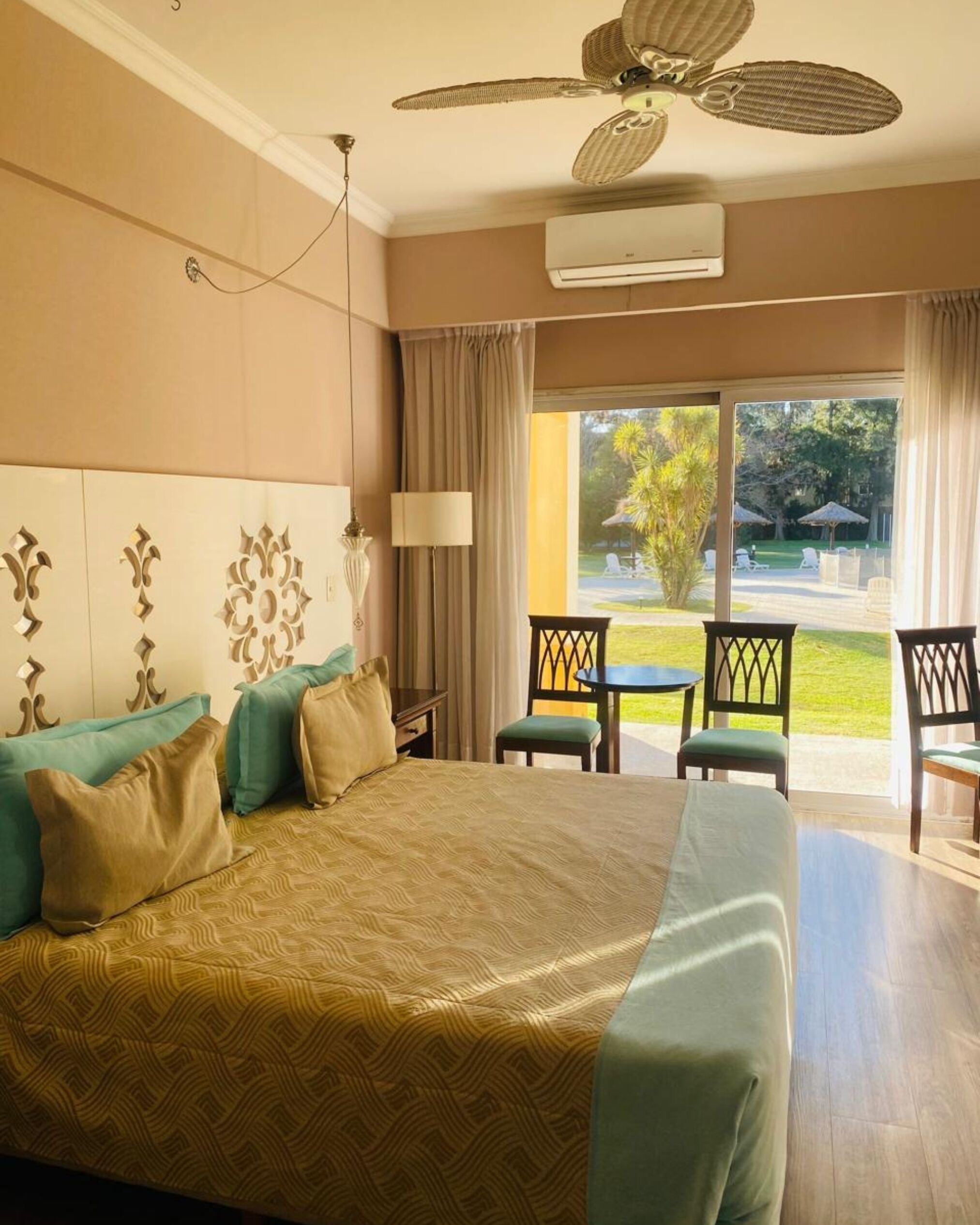 Una habitación de hotel con una cama grande, ventilador de techo, aire acondicionado, vistas al exterior y un comedor con sillas y una mesa.