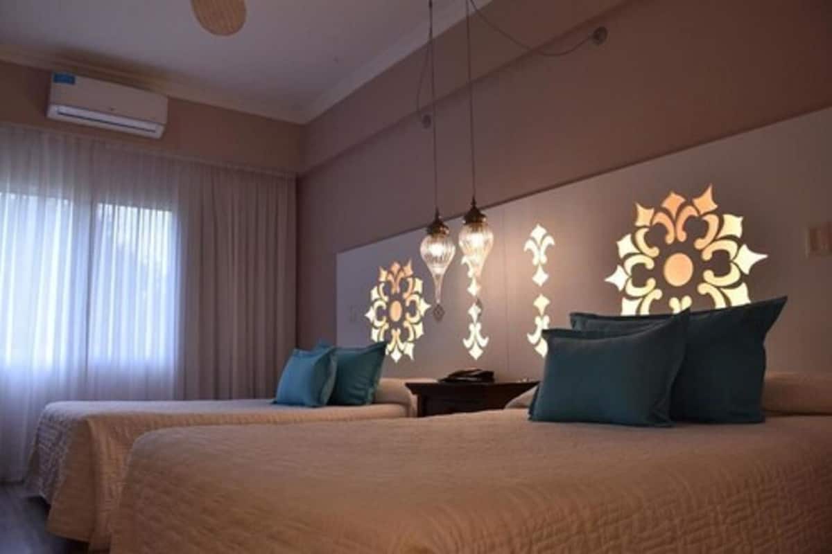 Une chambre d’hôtel avec deux lits, un climatiseur fixé au mur et des appliques murales décoratives.