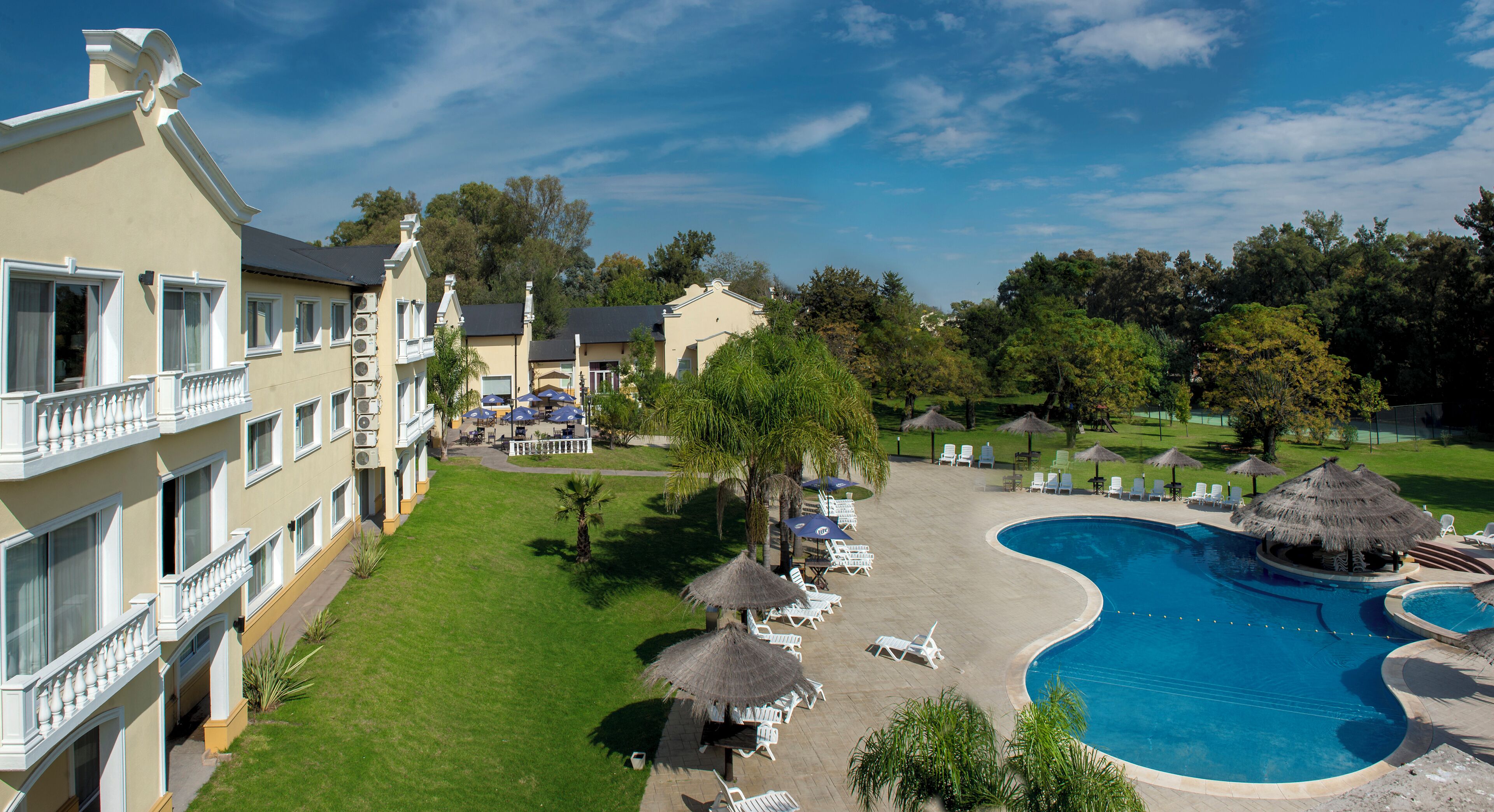 A hotel with a swimming pool, lounge chairs, and a well-maintained lawn.